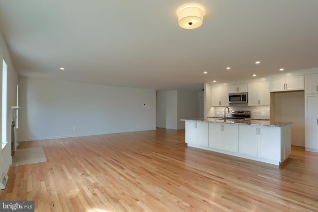 kitchen with light stone countertops, white cabinetry, stainless steel appliances, and light wood-type flooring