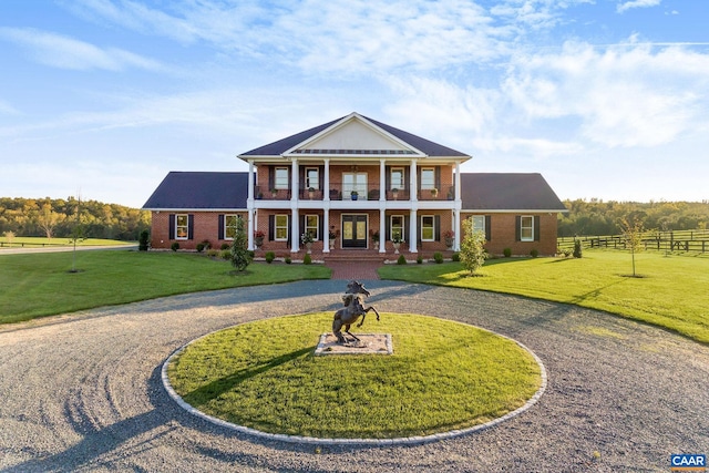 neoclassical home featuring a front yard, covered porch, and a balcony