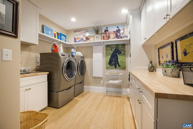 laundry room with washing machine and dryer, cabinets, and light wood-type flooring