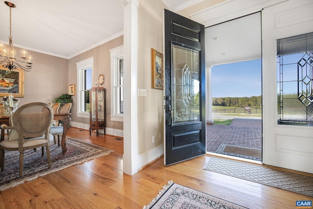 entryway with a notable chandelier, ornamental molding, and light wood-type flooring