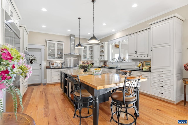 kitchen featuring wall chimney exhaust hood, white cabinetry, decorative light fixtures, and light hardwood / wood-style floors