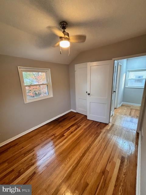 unfurnished bedroom featuring lofted ceiling, a textured ceiling, light wood-type flooring, and ceiling fan