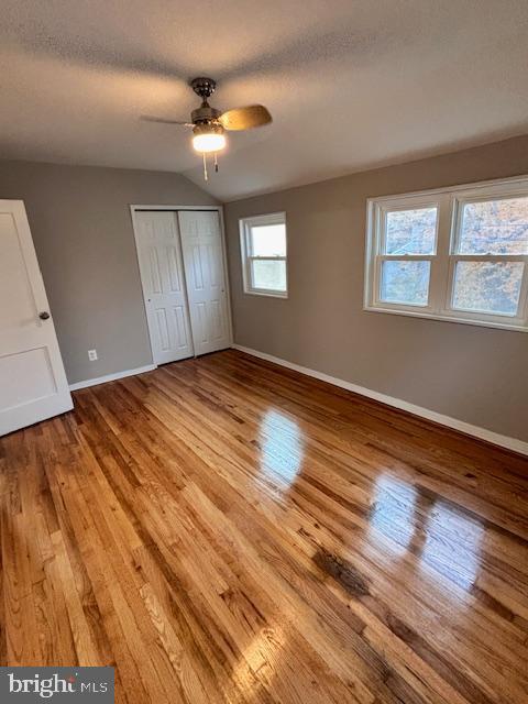 unfurnished bedroom featuring ceiling fan, a textured ceiling, vaulted ceiling, light hardwood / wood-style flooring, and a closet