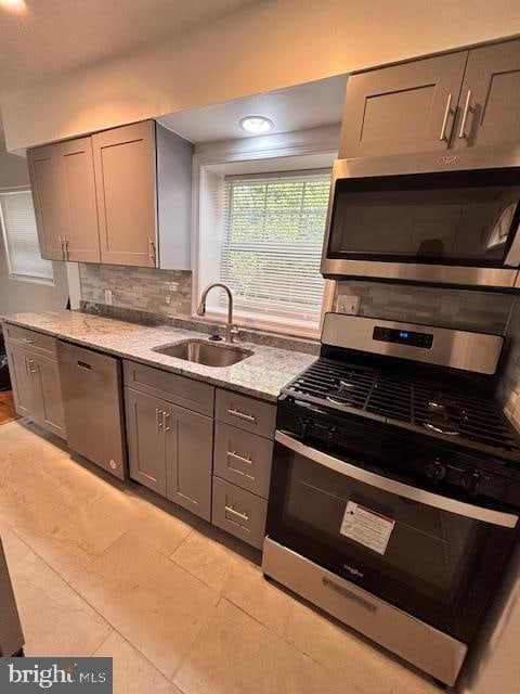 kitchen with backsplash, light stone countertops, sink, gray cabinetry, and stainless steel appliances