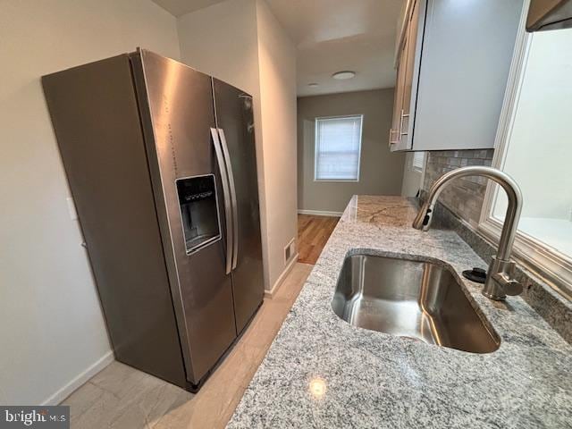 kitchen with sink, light wood-type flooring, light stone counters, decorative backsplash, and stainless steel refrigerator with ice dispenser