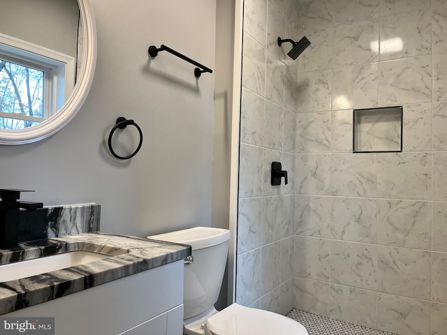 bathroom featuring a tile shower, vanity, and toilet