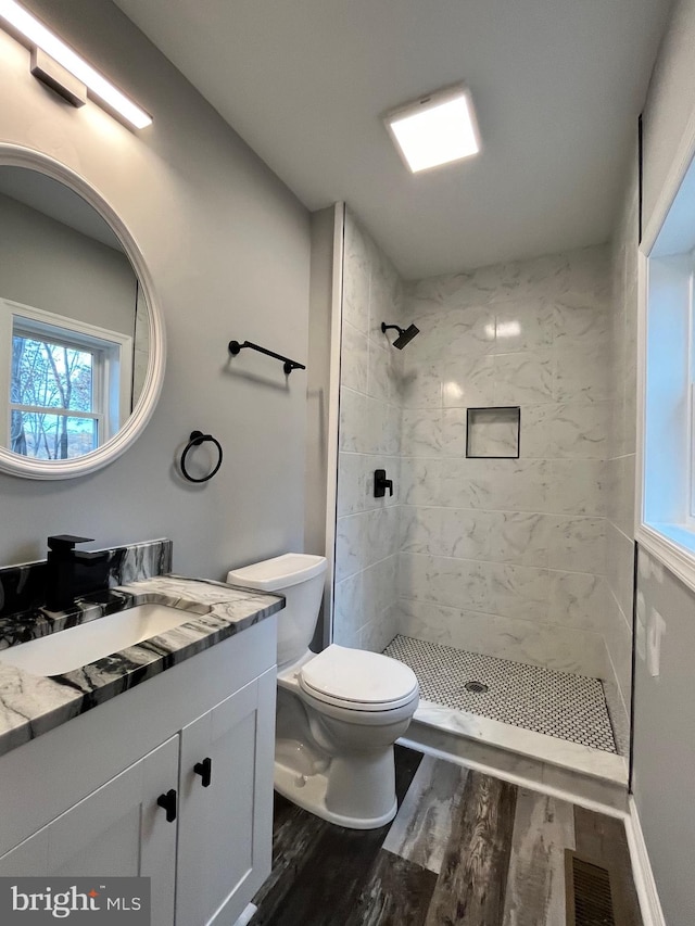 bathroom with a tile shower, toilet, vanity, and hardwood / wood-style flooring