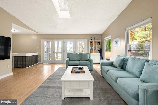 living room with lofted ceiling with skylight, hardwood / wood-style floors, french doors, and a textured ceiling