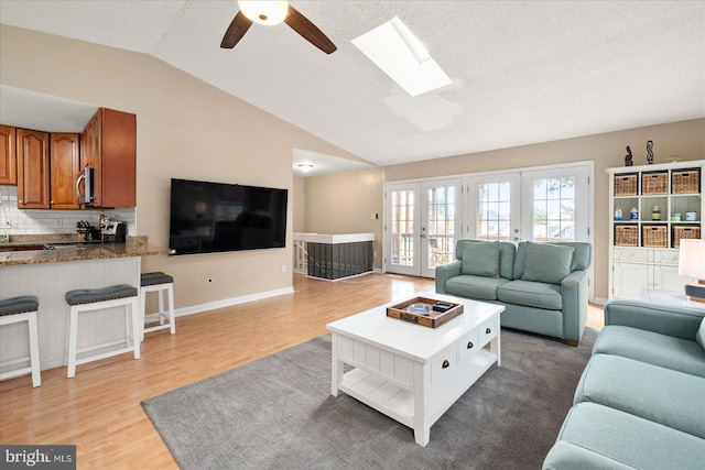 living room with light hardwood / wood-style floors, vaulted ceiling with skylight, ceiling fan, a textured ceiling, and french doors