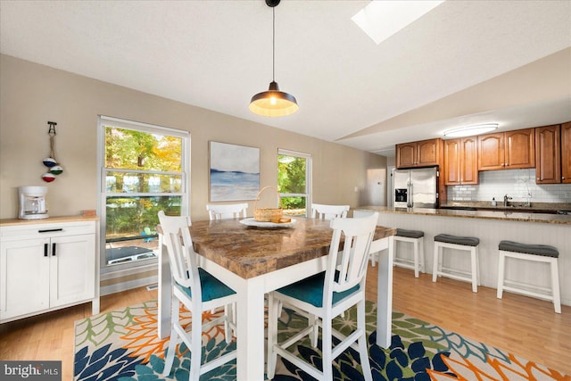 dining space featuring light hardwood / wood-style flooring and lofted ceiling with skylight