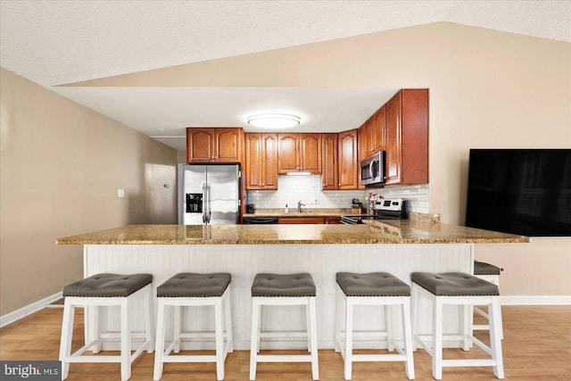 kitchen featuring stainless steel appliances, kitchen peninsula, light wood-type flooring, and vaulted ceiling