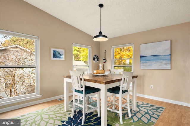 dining room featuring a textured ceiling, light wood-type flooring, and lofted ceiling