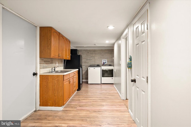 kitchen with black refrigerator, sink, washer and clothes dryer, backsplash, and light wood-type flooring