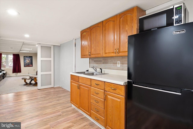 kitchen with light hardwood / wood-style floors, black fridge, decorative backsplash, and sink