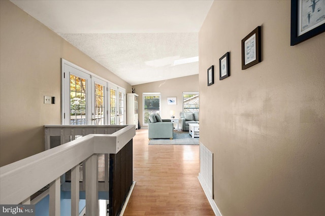 hall featuring french doors, light hardwood / wood-style flooring, lofted ceiling, and a healthy amount of sunlight