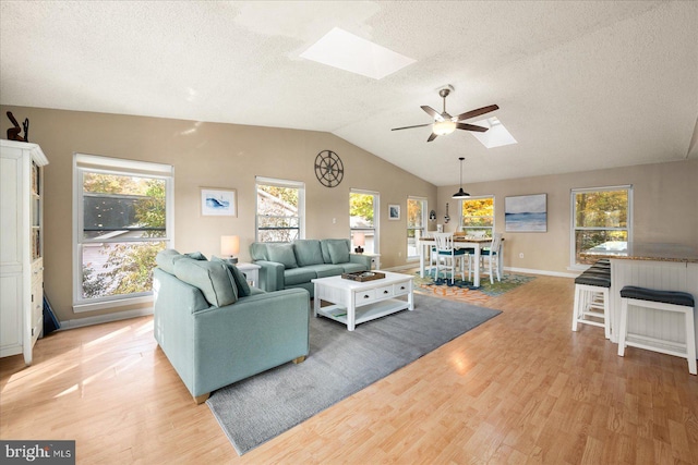 living room featuring a textured ceiling, light hardwood / wood-style floors, ceiling fan, and lofted ceiling with skylight