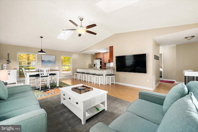 living room featuring vaulted ceiling with skylight, ceiling fan, and wood-type flooring