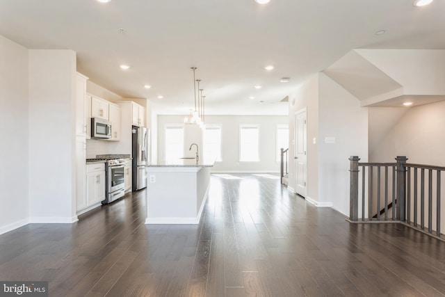 kitchen with stainless steel appliances, white cabinets, hanging light fixtures, and an island with sink