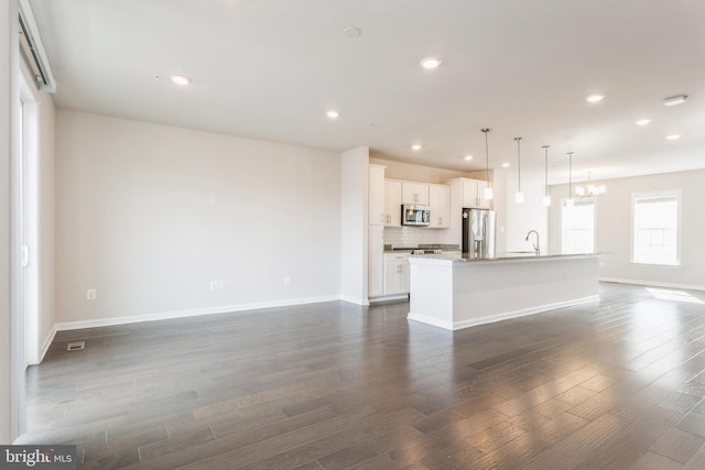 unfurnished living room featuring recessed lighting, a sink, baseboards, dark wood finished floors, and an inviting chandelier