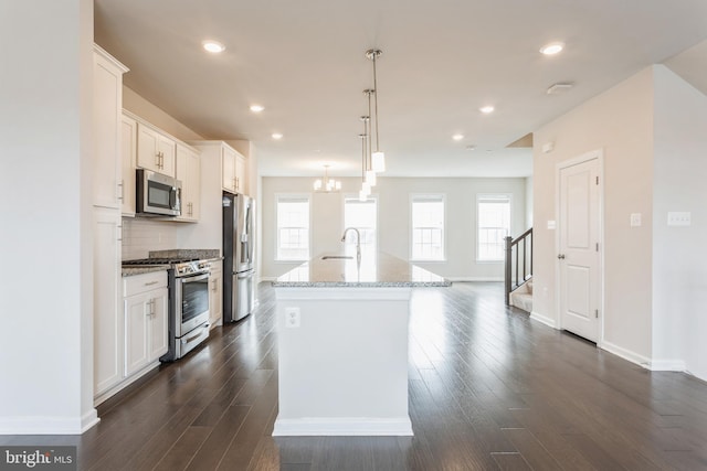 kitchen with a kitchen island with sink, stainless steel appliances, a sink, white cabinets, and pendant lighting