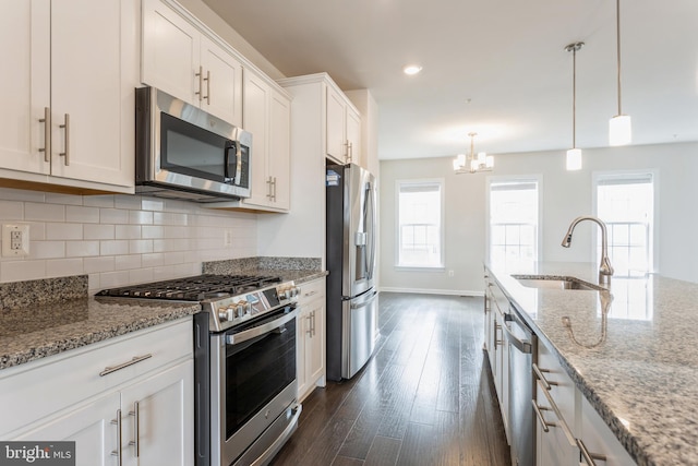 kitchen featuring light stone counters, stainless steel appliances, a sink, white cabinetry, and pendant lighting