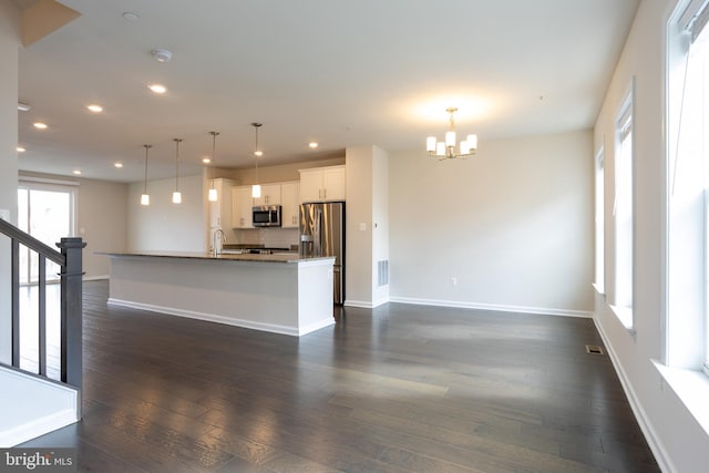 kitchen featuring dark wood-style flooring, decorative light fixtures, stainless steel appliances, a kitchen island with sink, and white cabinetry