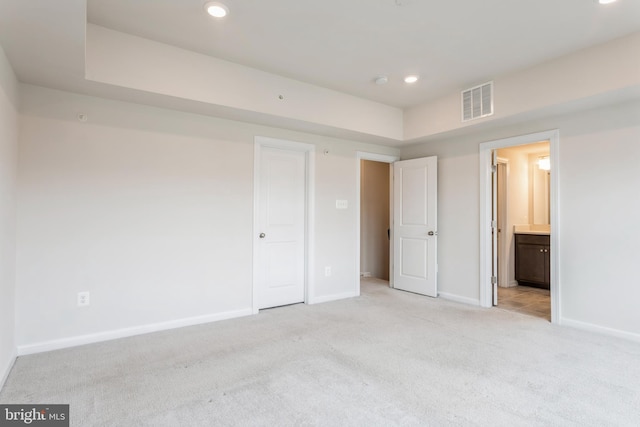 unfurnished bedroom with recessed lighting, light colored carpet, visible vents, ensuite bath, and baseboards