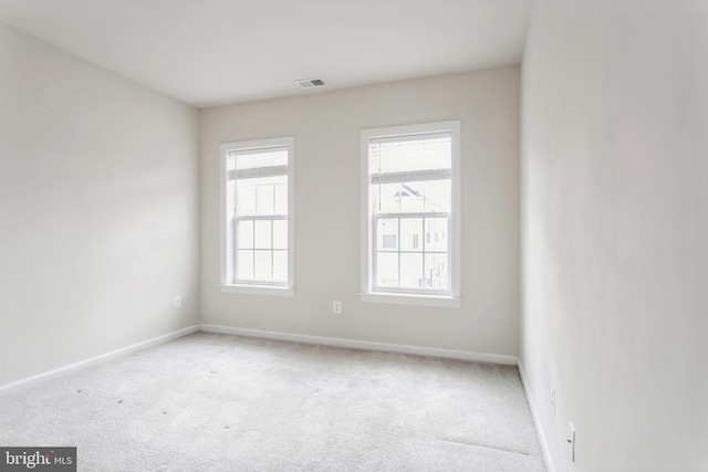 spare room featuring light colored carpet, visible vents, and baseboards