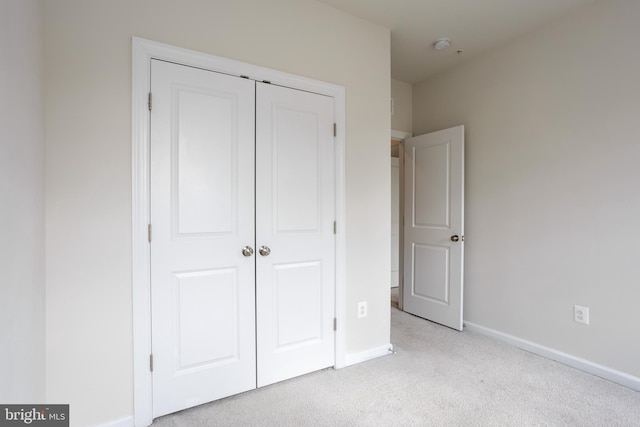 unfurnished bedroom featuring baseboards, a closet, and light colored carpet