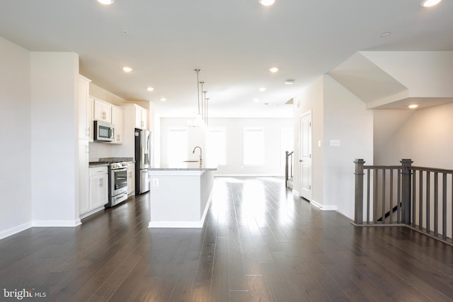 kitchen with stainless steel appliances, white cabinets, a kitchen island with sink, and decorative light fixtures