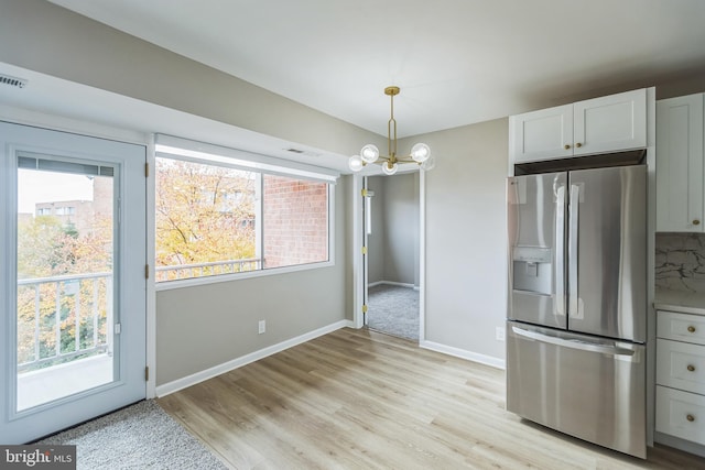 kitchen with white cabinetry, light wood-type flooring, a chandelier, stainless steel fridge, and pendant lighting