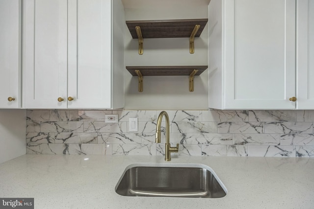 kitchen with white cabinets, decorative backsplash, sink, and light stone countertops