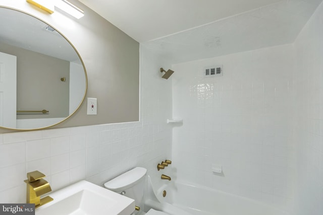 bathroom with toilet, tiled shower / bath combo, and tile walls