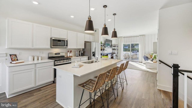 kitchen with a center island with sink, white cabinets, decorative light fixtures, appliances with stainless steel finishes, and dark hardwood / wood-style flooring