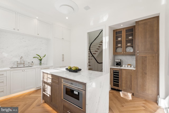 kitchen with sink, decorative backsplash, white cabinetry, beverage cooler, and light parquet flooring