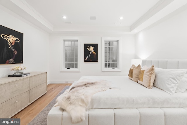 bedroom with a raised ceiling, light hardwood / wood-style floors, and ornamental molding