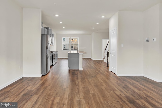 kitchen with a center island with sink, appliances with stainless steel finishes, pendant lighting, and dark hardwood / wood-style flooring