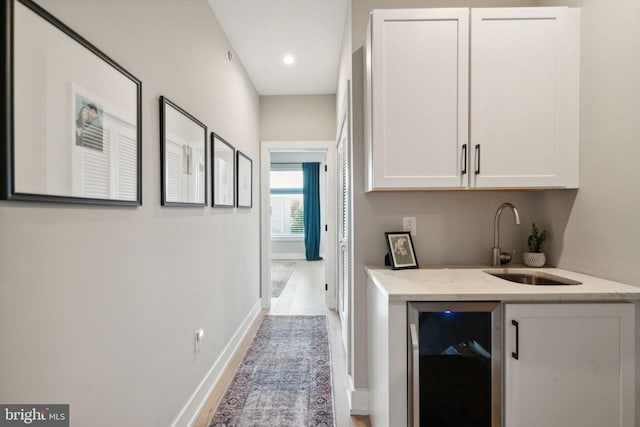 bar featuring light hardwood / wood-style flooring, sink, light stone countertops, beverage cooler, and white cabinets