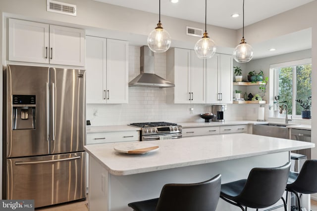 kitchen featuring wall chimney range hood, sink, light stone countertops, white cabinetry, and appliances with stainless steel finishes