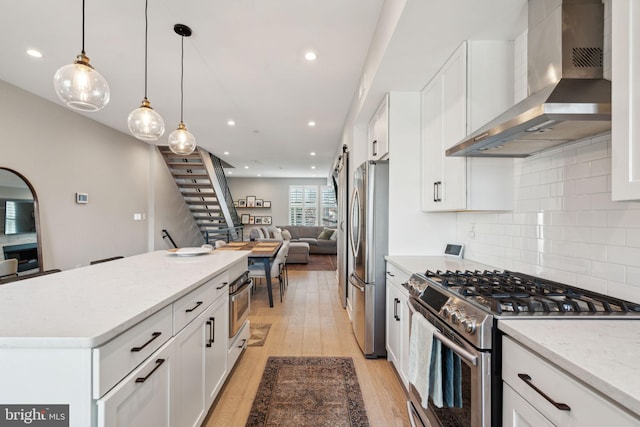 kitchen featuring wall chimney range hood, light hardwood / wood-style flooring, white cabinets, and stainless steel appliances