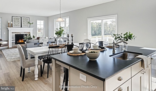 kitchen with a stone fireplace, white cabinets, sink, pendant lighting, and light wood-type flooring