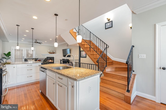 kitchen with white cabinets, light wood-type flooring, an island with sink, and sink