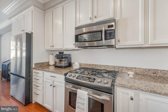 kitchen featuring light stone countertops, backsplash, stainless steel appliances, light hardwood / wood-style flooring, and white cabinets