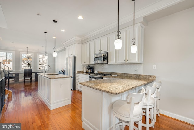 kitchen with kitchen peninsula, appliances with stainless steel finishes, light wood-type flooring, decorative light fixtures, and white cabinetry