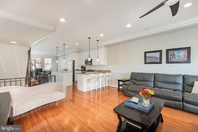 living room with ceiling fan with notable chandelier, light wood-type flooring, and crown molding