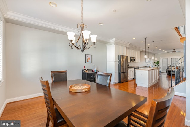 dining room with ceiling fan with notable chandelier, light wood-type flooring, ornamental molding, and sink