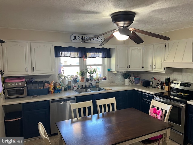 kitchen with a textured ceiling, sink, custom exhaust hood, white cabinetry, and appliances with stainless steel finishes