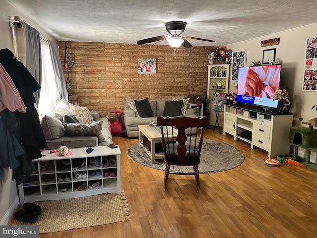 living room featuring wooden walls, wood-type flooring, ceiling fan, and a textured ceiling