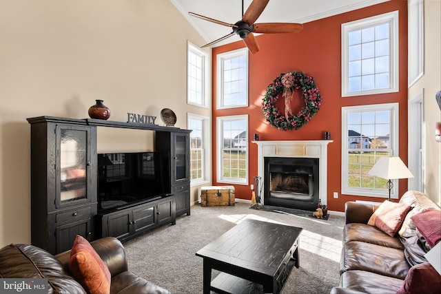 carpeted living room with plenty of natural light, ceiling fan, a towering ceiling, and crown molding