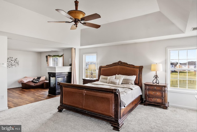 bedroom featuring carpet flooring, ceiling fan, a multi sided fireplace, and multiple windows